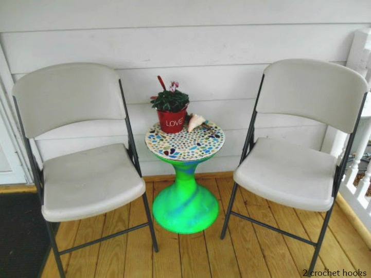 Finished sea glass mosaic table top next to two folding chairs.