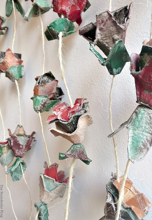 Egg carton flowers strung together and hanging as wall art against a neutral beige wall.