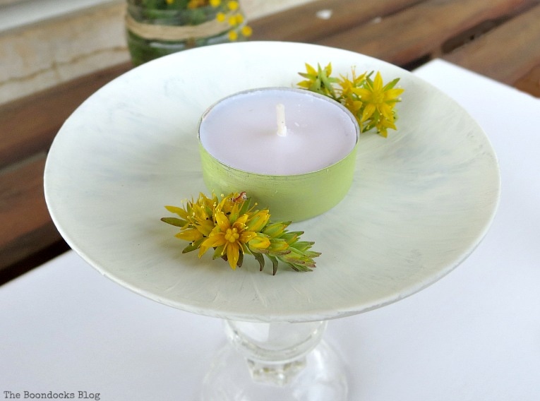 Painted tealight with yellow succulent flowers sitting on the painted saucer.