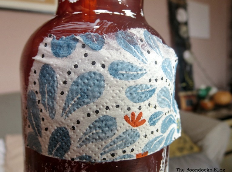 Close up of decoupaged three ply napkin on a brown plastic bottle.