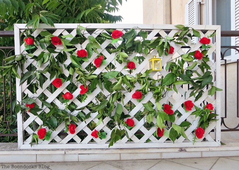 Finished lattice flower wall with red roses, greenery and yellow lantern.