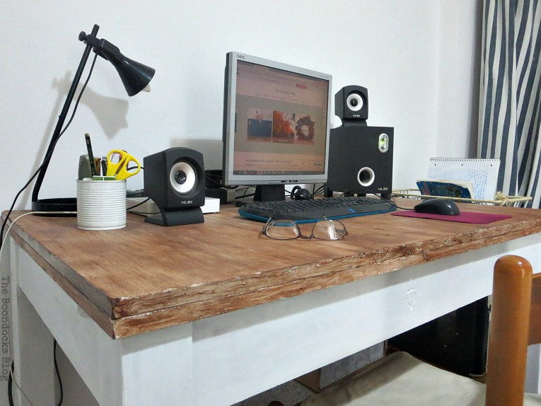 Wood desk with computer, black lamp, glasses, speakers and pen holder placed on top.