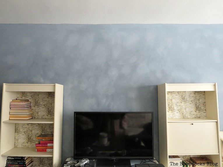 Two shelves and a TV placed infront of an accent wall with cloudy effect.