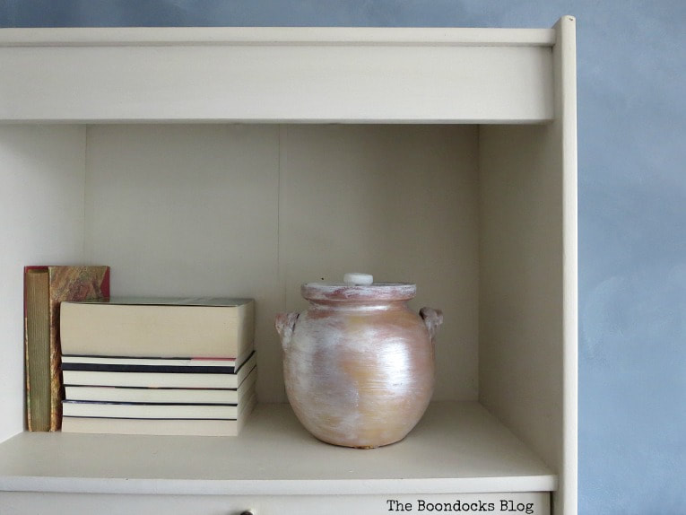 White bookcase with off white backing and books and painted pot placed on the shelf.