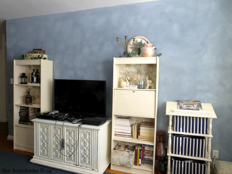 Finished living room with furniture, TV and bookcases placed in front of the cloudy painted accent wall.