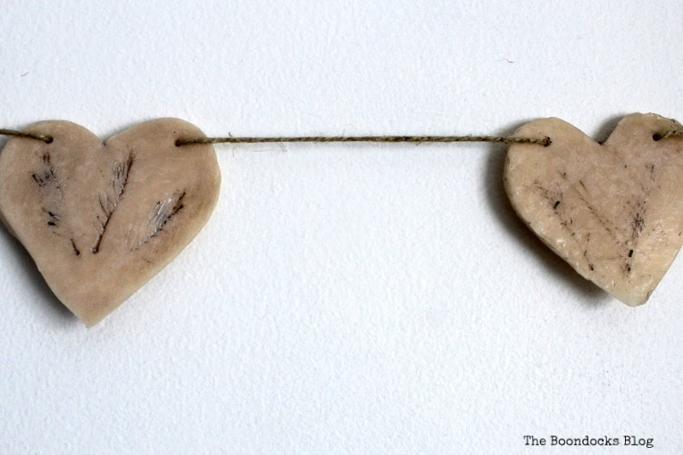 Two clay hearts hung from twine, How to Make a Natural Clay Valentine's Heart Garland www.theboondocksblog.com
