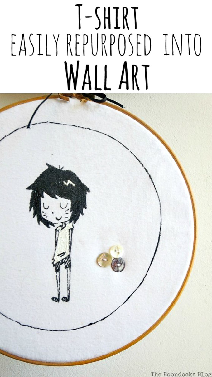 Close up of hoop wall art made from an upcycled tshirt. It shows a girl character and three sewn on buttons and text overlay "T-shirt easily repurposed into wall art"